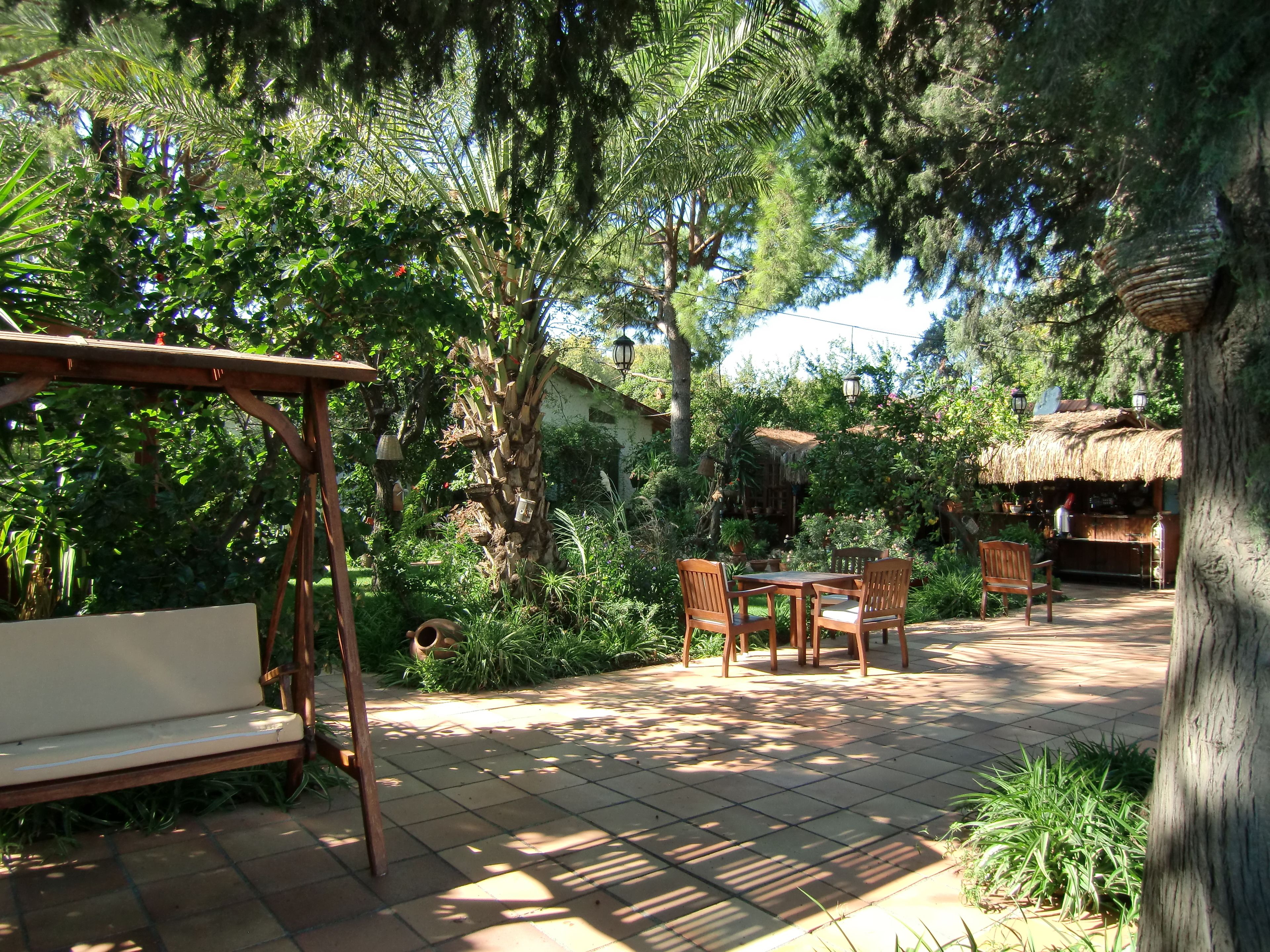 A patio area with a wooden swing set, a table with chairs, and a thatched-roof structure.