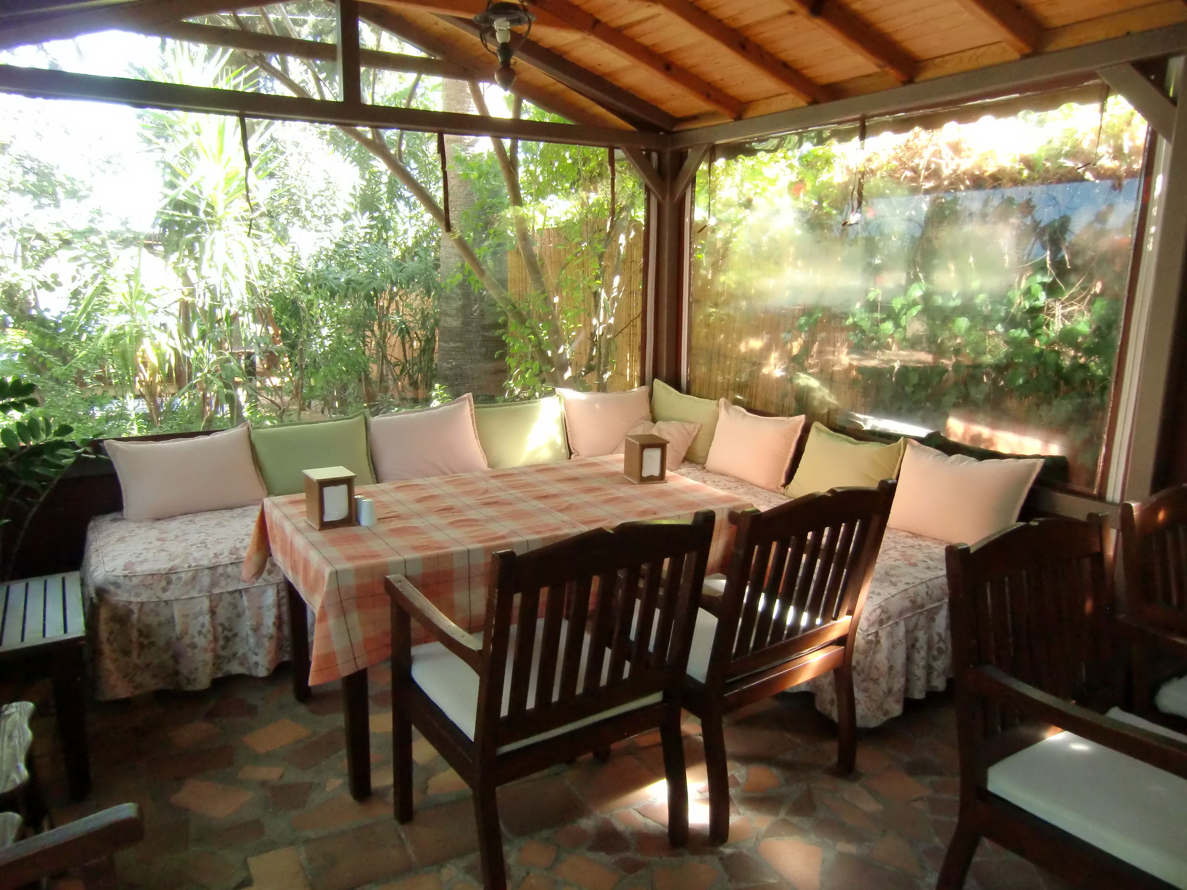 Een overdekt terras met een tafel en stoelen, omringd door weelderige begroeiing.