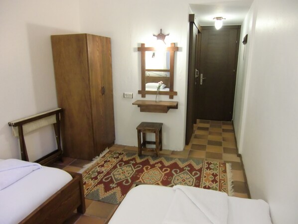 Un dormitorio con un armario de madera, una mesita pequeña, un espejo y una alfombra estampada.