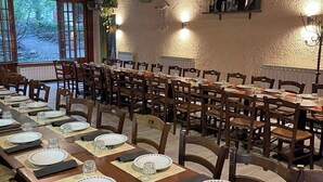 Una larga mesa de comedor dispuesta con sillas, vigas de madera y ventanas con vistas a la vegetación.