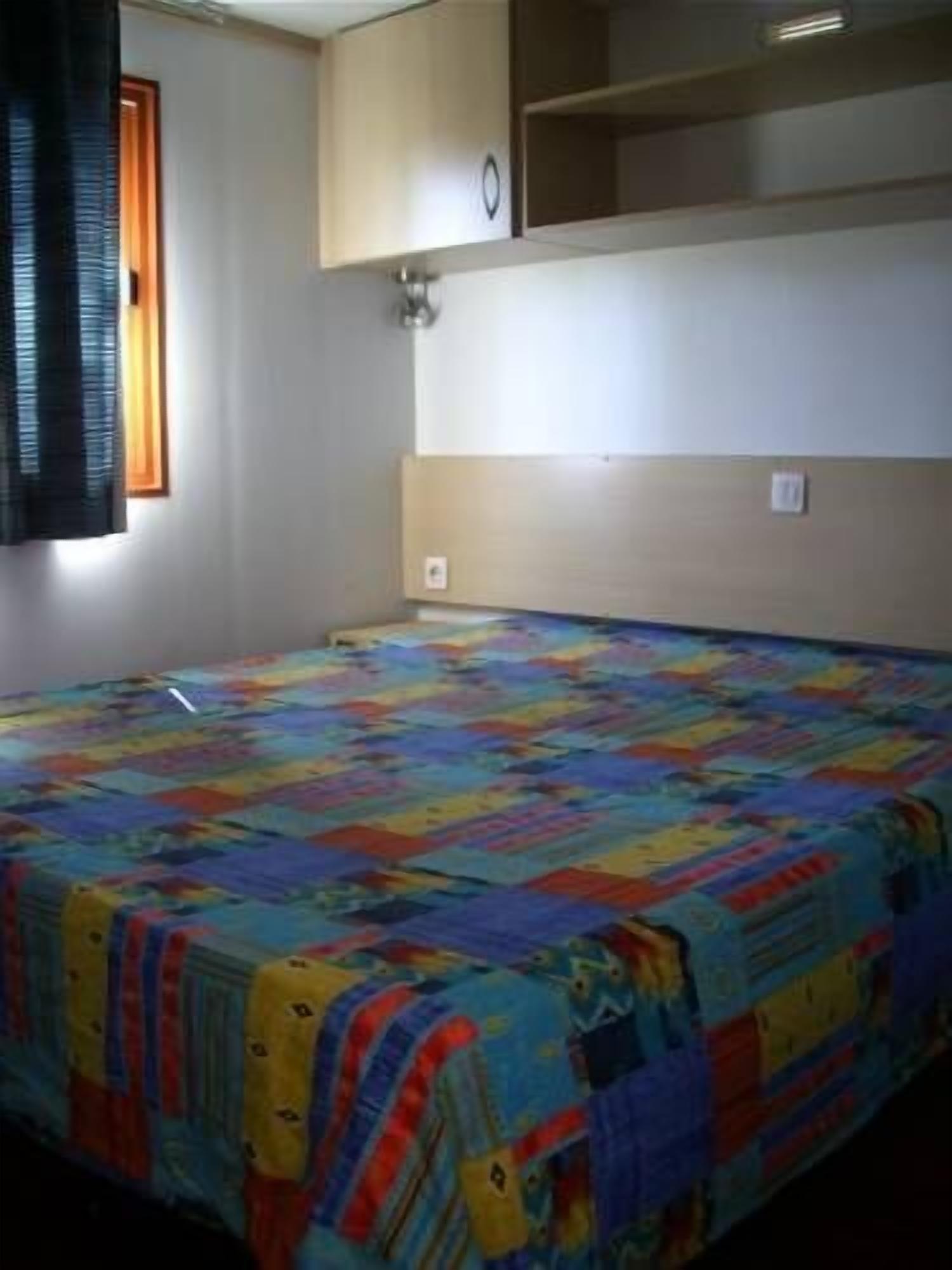 A bedroom with a colorful quilt, a window with blinds, and built-in shelving.