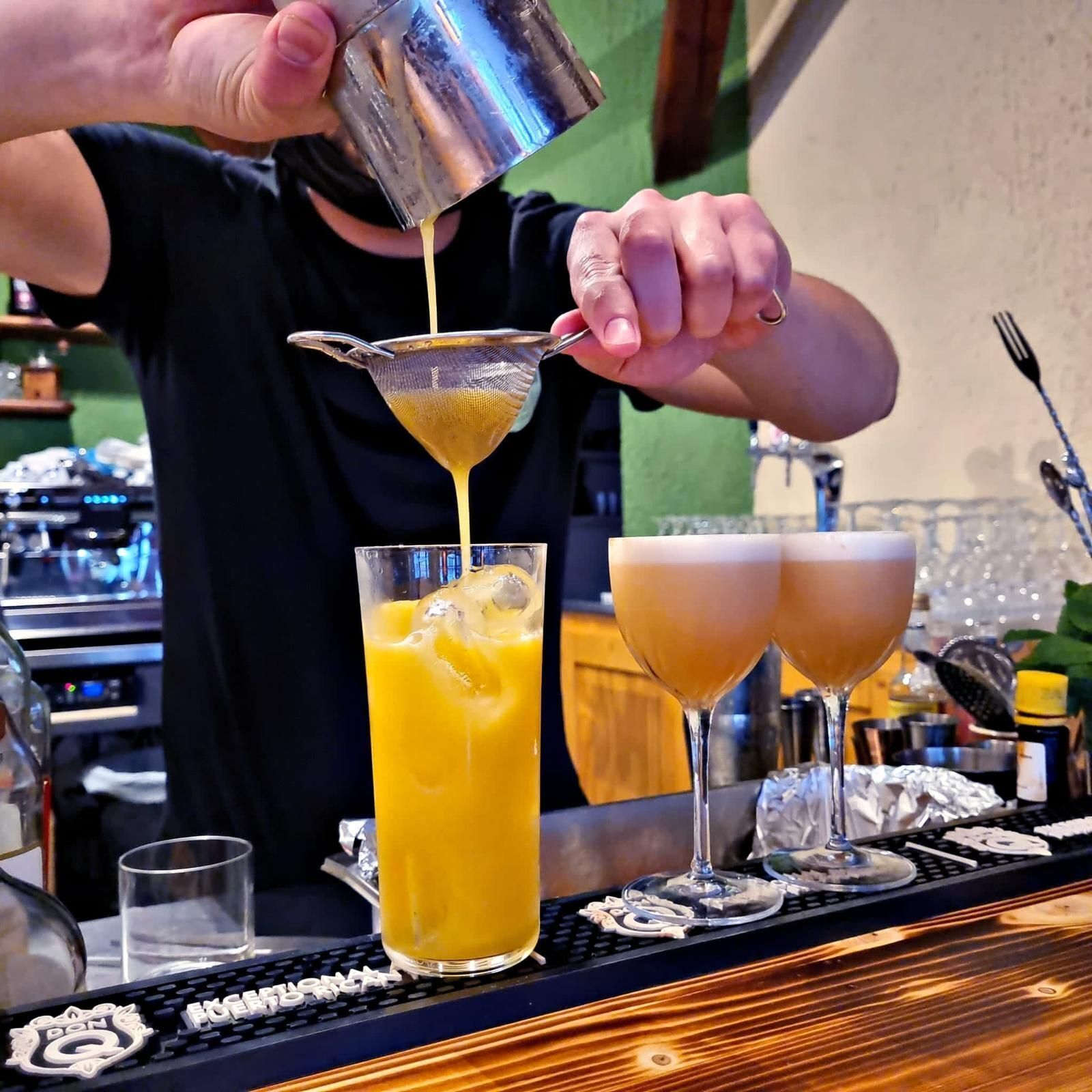 A bartender pouring a yellow liquid into a tall glass.
