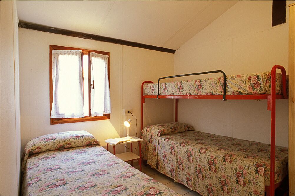 Une chambre de dortoir avec des lits superposés, un petit bureau avec une lampe et une fenêtre avec des rideaux.