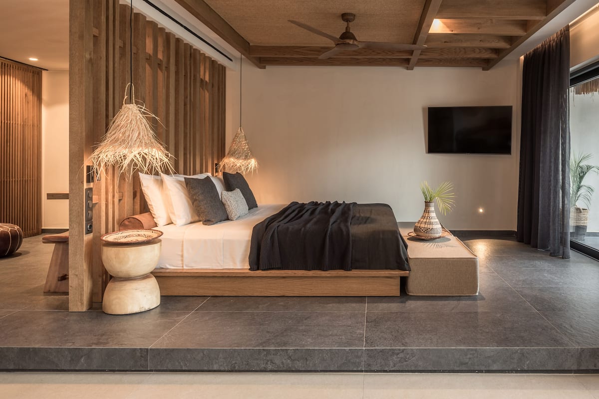 Un dormitorio moderno con una cama grande, detalles de madera, un ventilador de techo y un televisor en la pared.