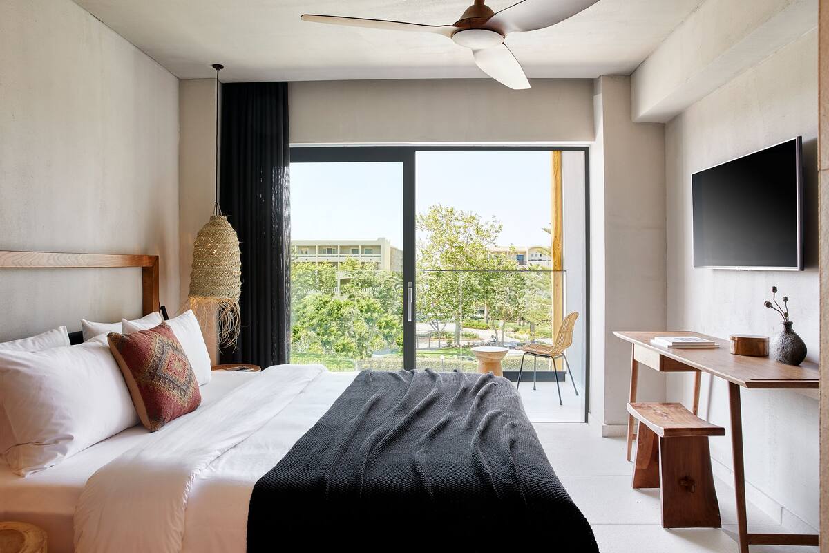 Una habitación de hotel moderna con una cama grande, un escritorio, un televisor y un balcón con vistas a la ciudad.