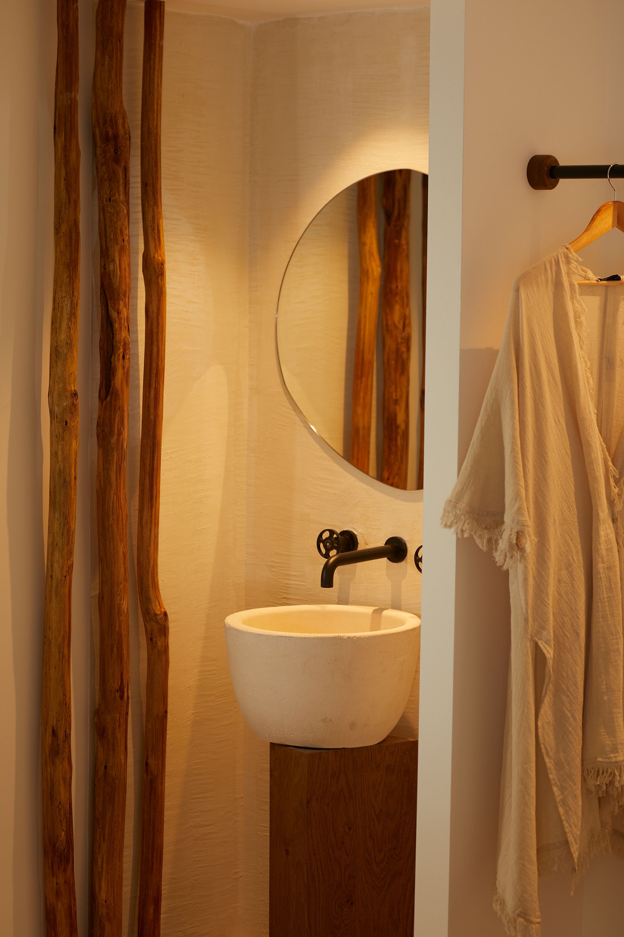 Un baño con pared de madera, un espejo redondo, un lavamanos blanco y un perchero para toallas.