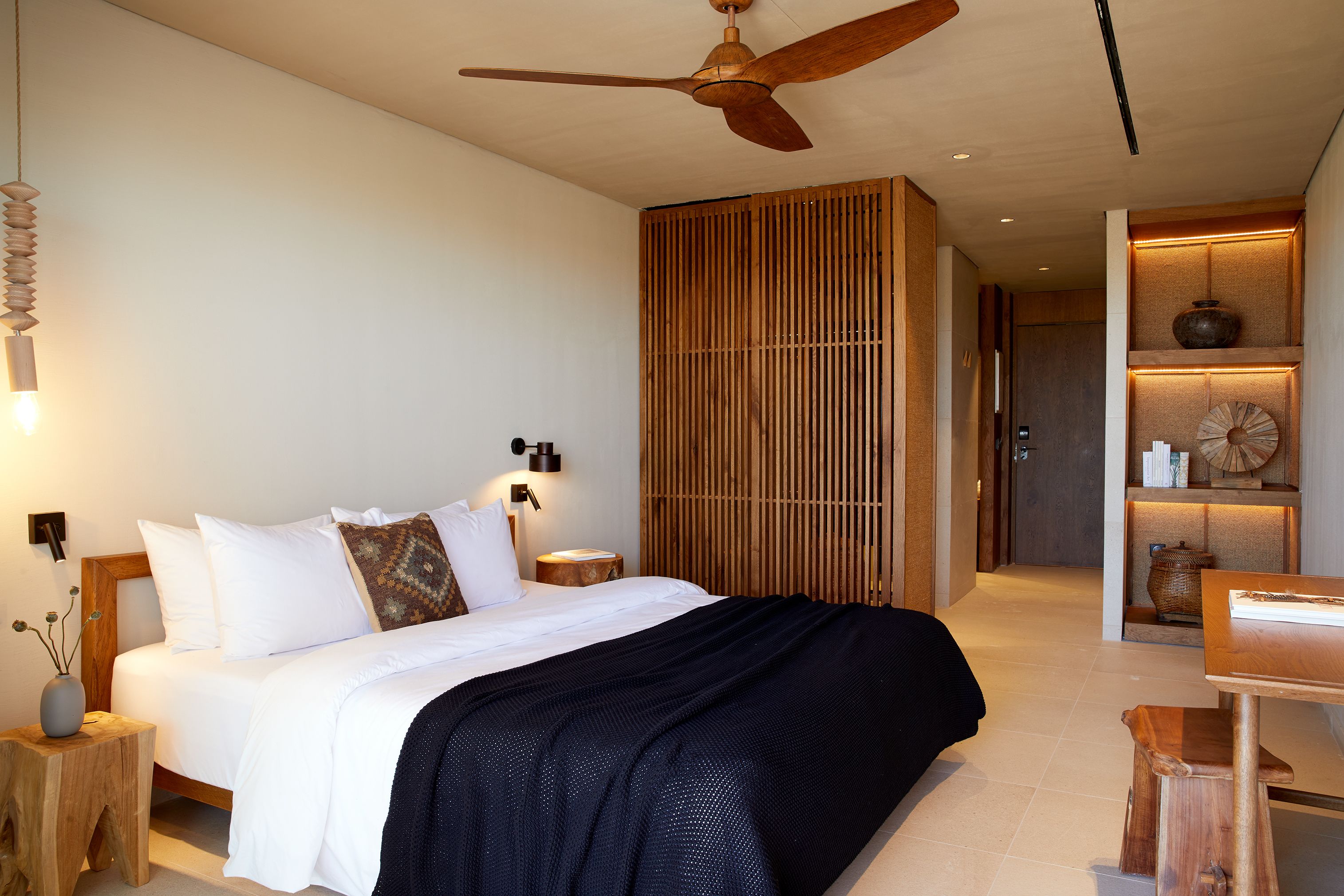 Un dormitorio moderno con una cama grande, un ventilador de techo, una mesita de noche con lámpara y un panel de pared de madera.