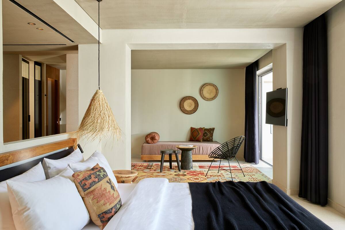 Una habitación de hotel moderna con una cama grande, una lámpara colgante, una mesita y un televisor en la pared.