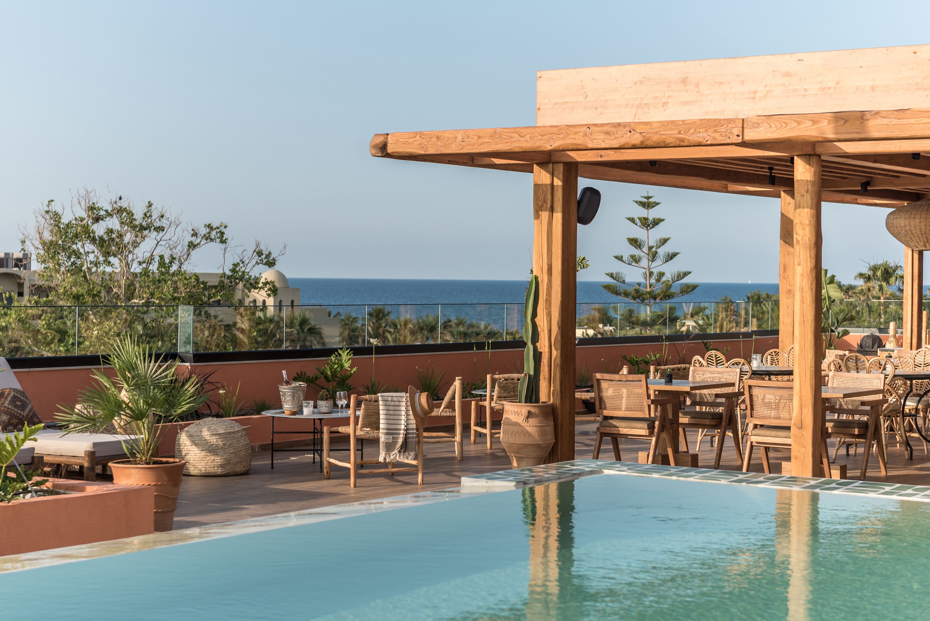 A rooftop pool area with lounge chairs and tables, overlooking a body of water.