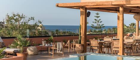 A rooftop pool area with lounge chairs and tables, overlooking a body of water.