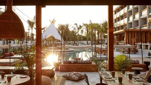 A poolside area with wooden furniture, a hanging light fixture, and a view of a building with a white facade and balconies. - The Syntopia Hotel (Rethymno)
