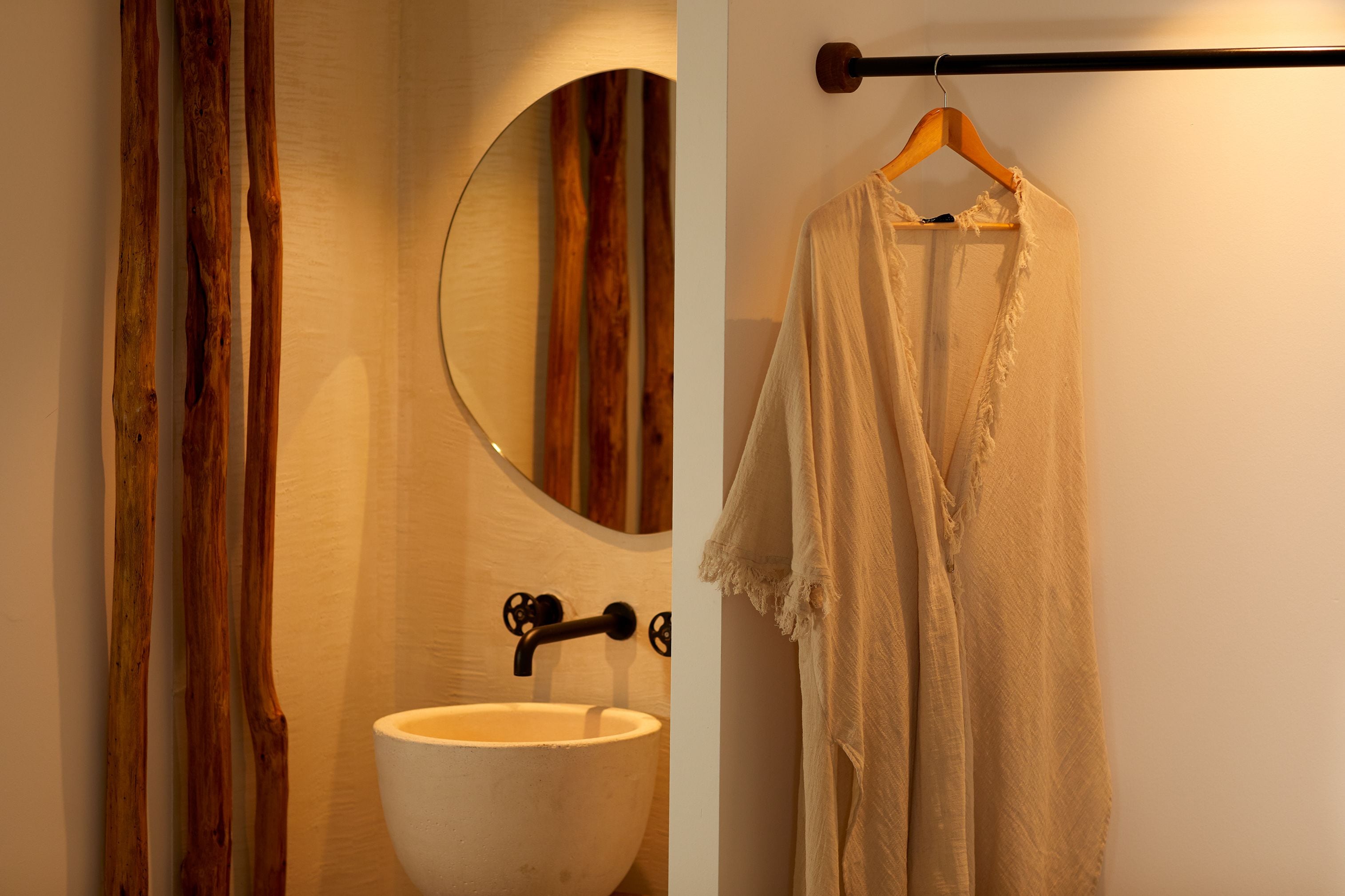 Un baño con pared de madera, un espejo redondo, un lavabo blanco y una toalla colgada en un perchero de madera.