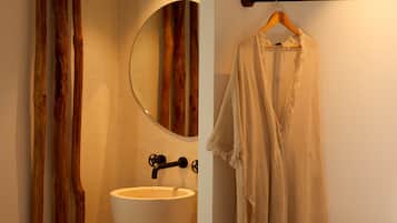 Un baño con pared de madera, un espejo redondo, un lavabo blanco y una toalla colgada en un perchero de madera.