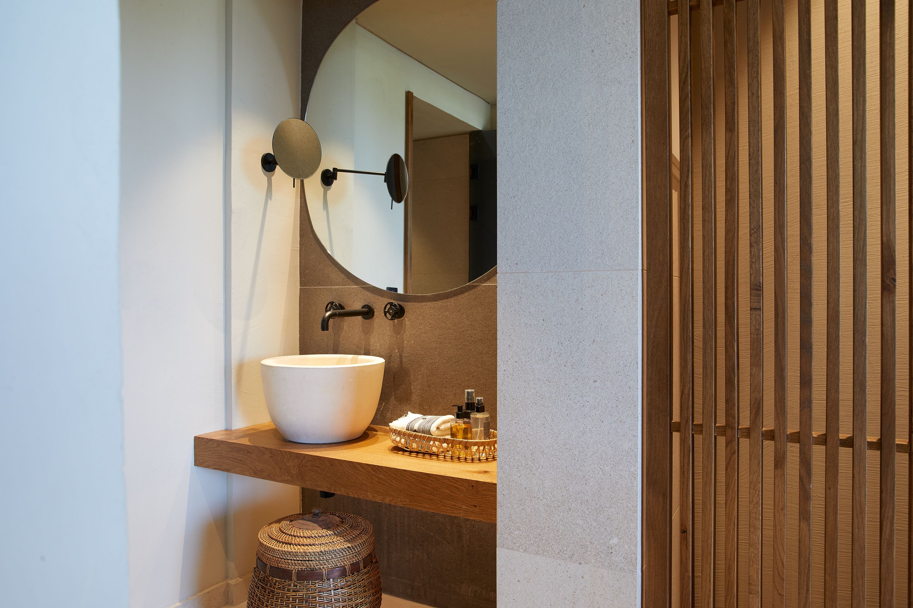 A bathroom with a large white basin, a mirror, and a wooden vanity.