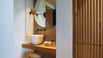 A bathroom with a large white basin, a mirror, and a wooden vanity.