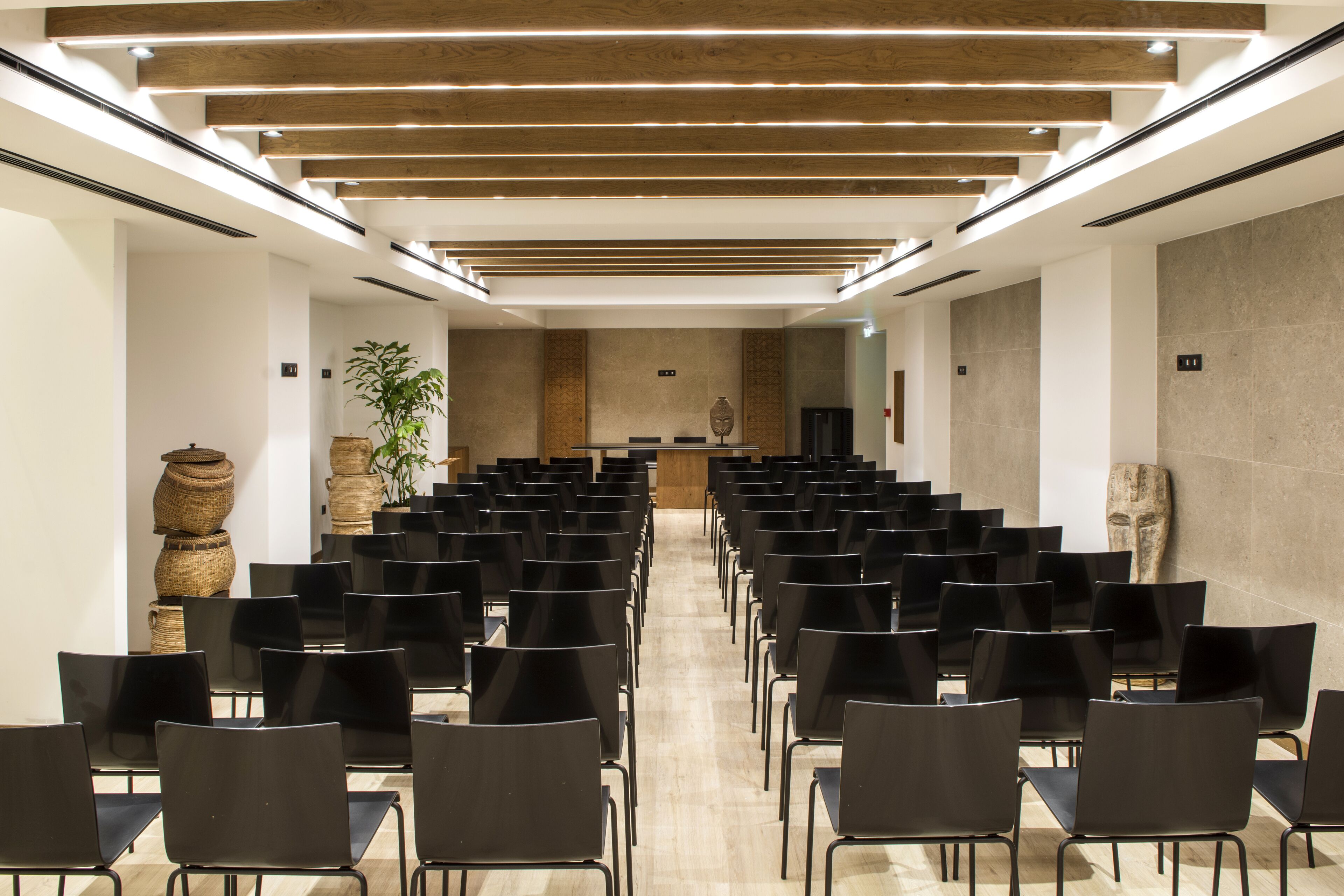 A conference room with rows of black chairs, wooden ceiling beams, and a central podium.