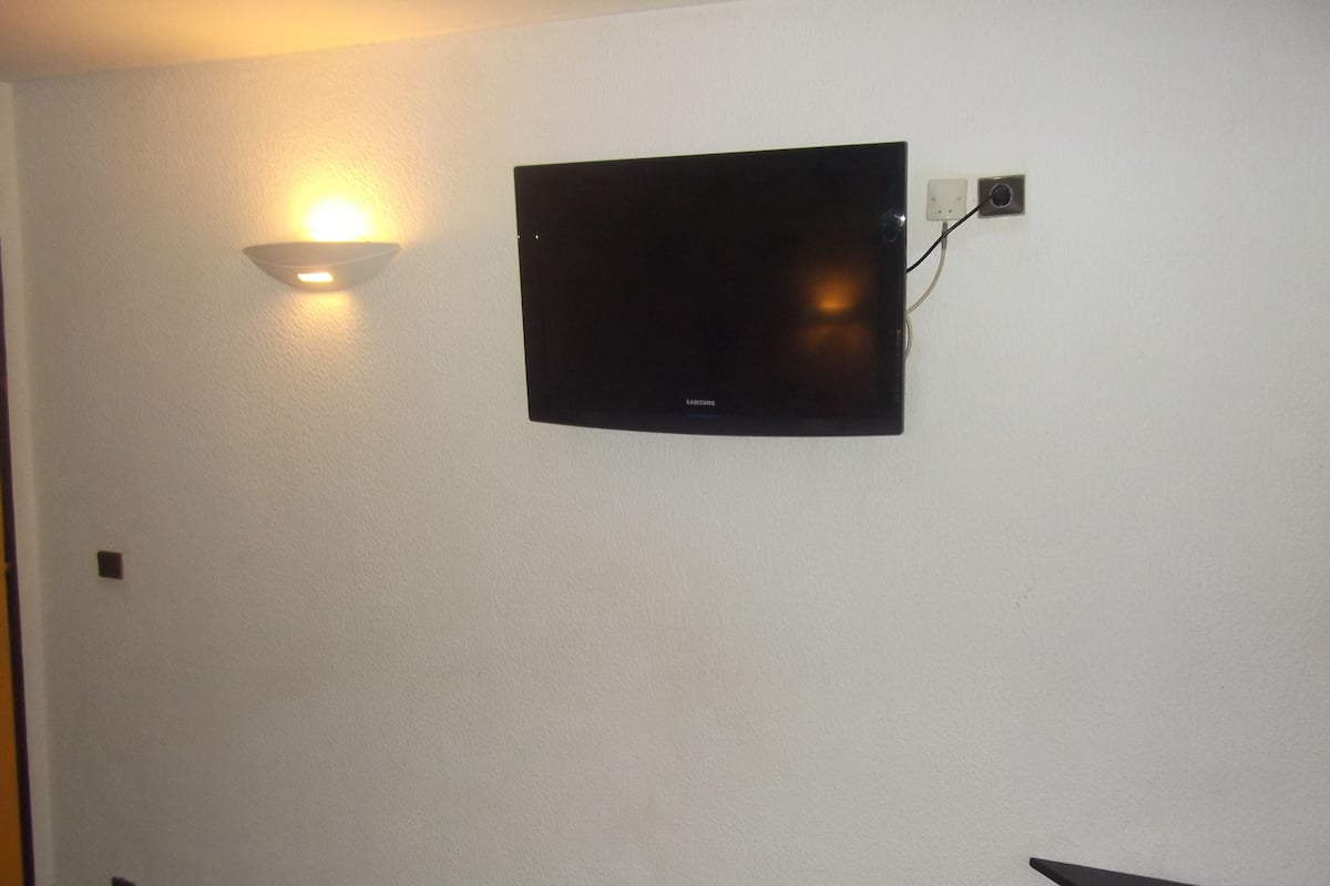 A wall-mounted flat-screen TV with a Samsung logo, a wall-mounted light fixture, and a power outlet.