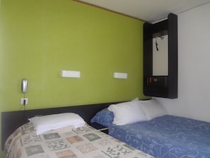 Ett hotellrum med två sängar, en grön vägg, en svart sänggavel och en väggmonterad TV.
