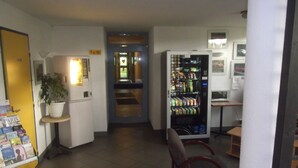 A hallway with a vending machine, a chair, a small table, and a potted plant. - Rev'Hotel Coignières (Coignieres)