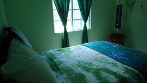 Un dormitorio con cama, una ventana con cortinas, una mesita de noche y un ventilador de pared.