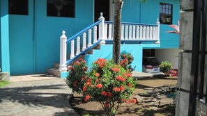 Un edificio con fachada azul, escalera blanca y flores rojas en primer plano.