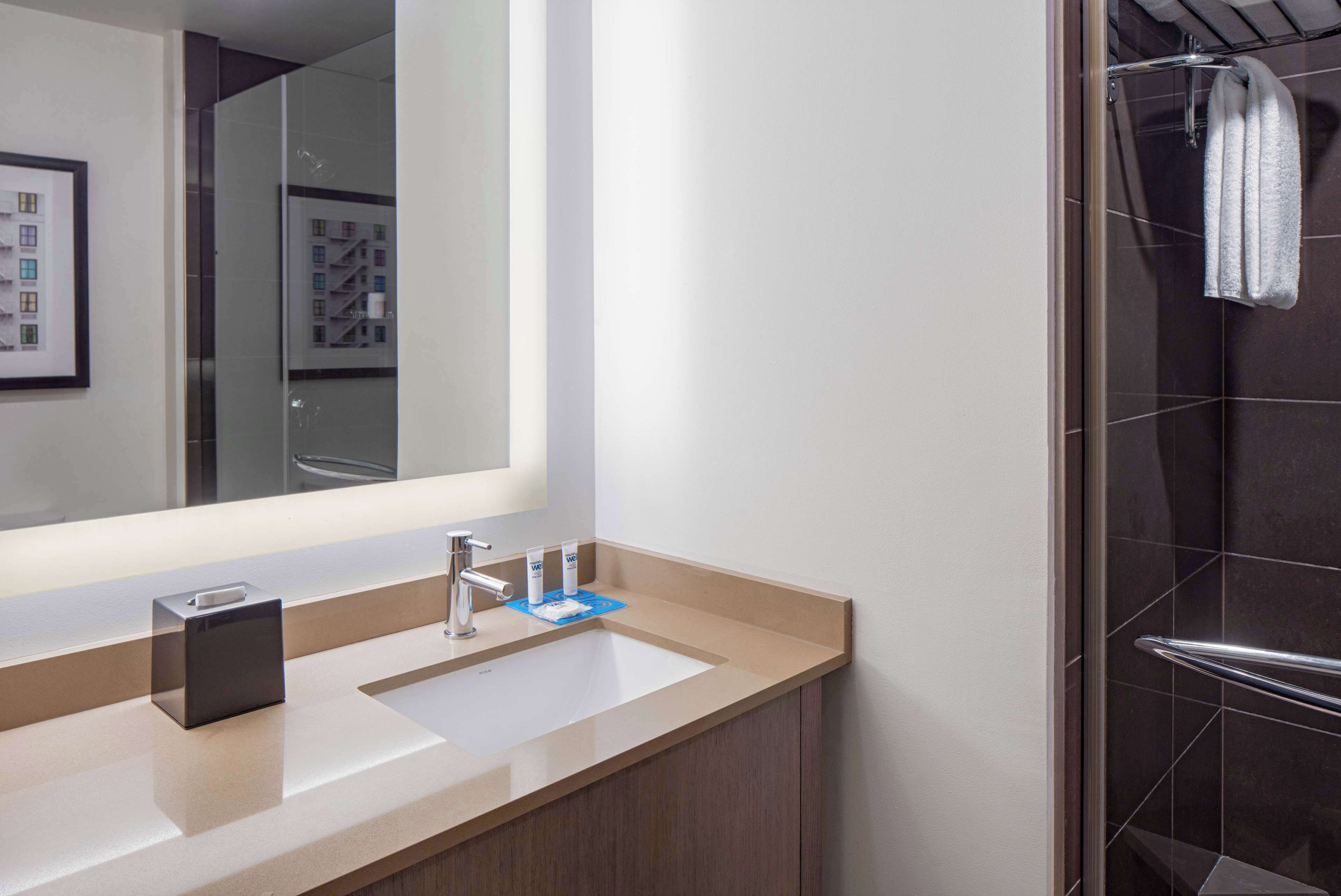 A modern bathroom with a large mirror, two sinks, and a shower area.