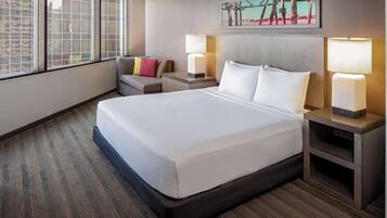 A hotel room with a large bed, two bedside tables with lamps, a small sofa with cushions, and a large window with a view.