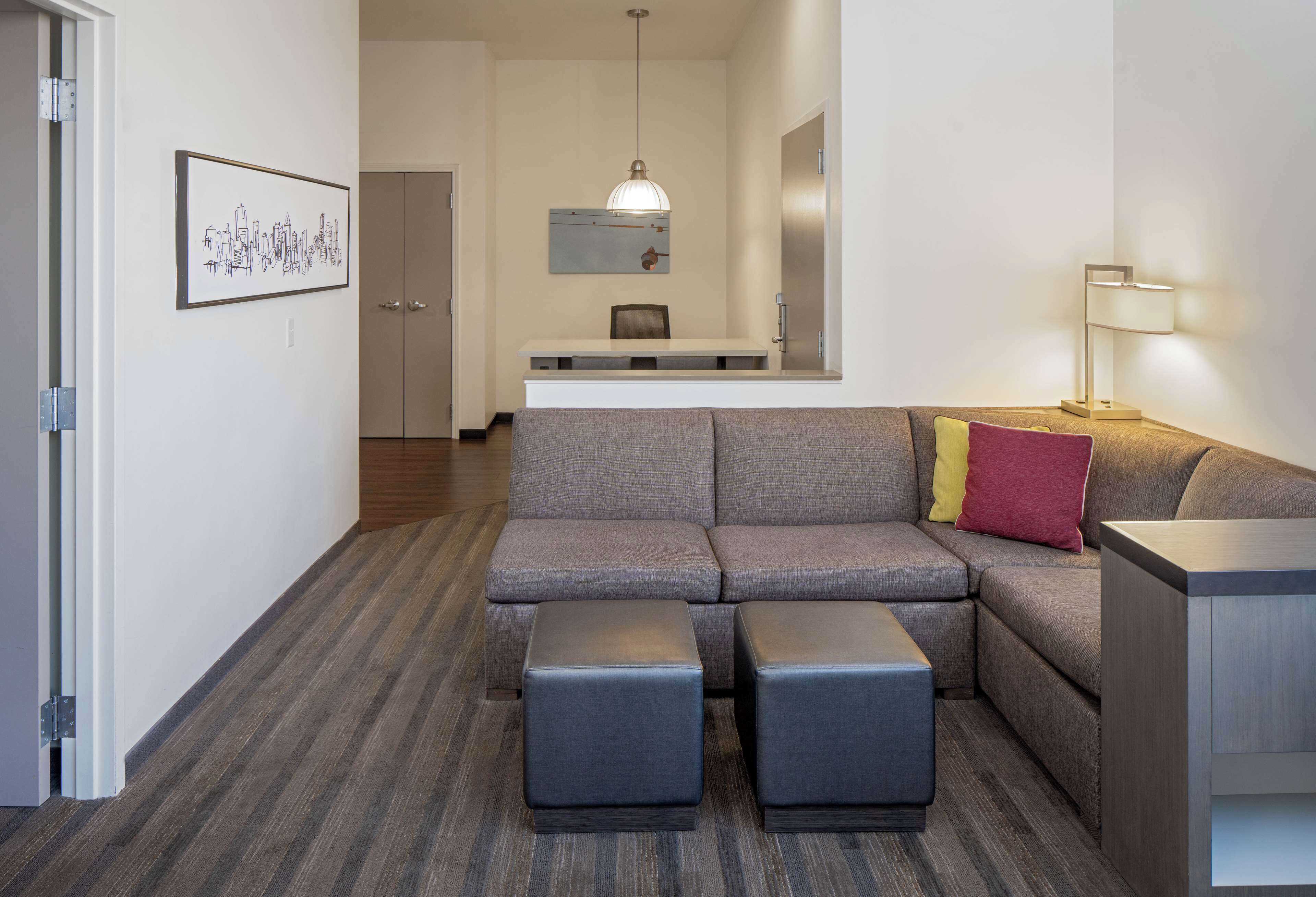 A modern living room with a sectional sofa, ottomans, a desk, and a pendant light.