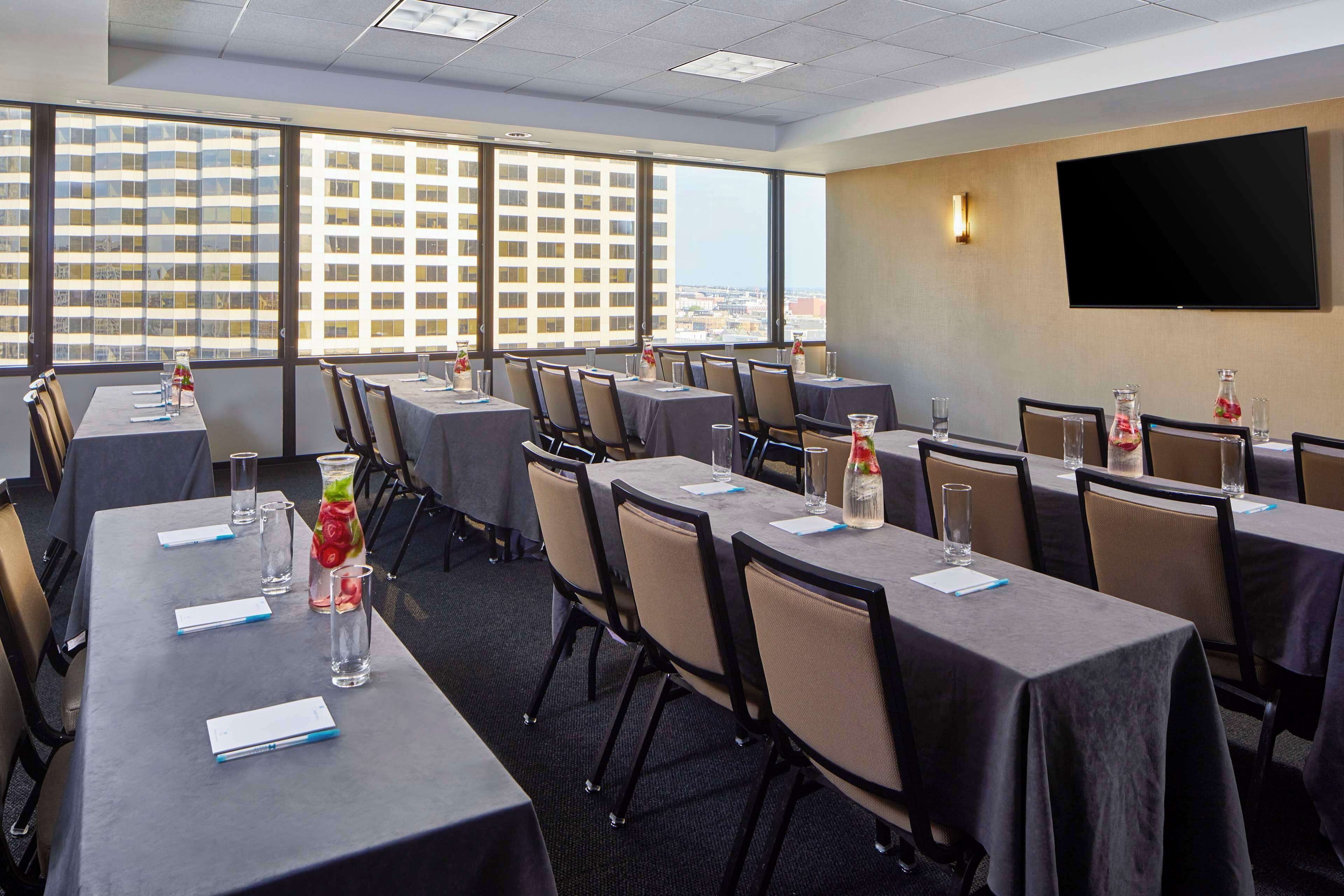 A conference room with multiple tables, chairs, and a large window offering a city view.