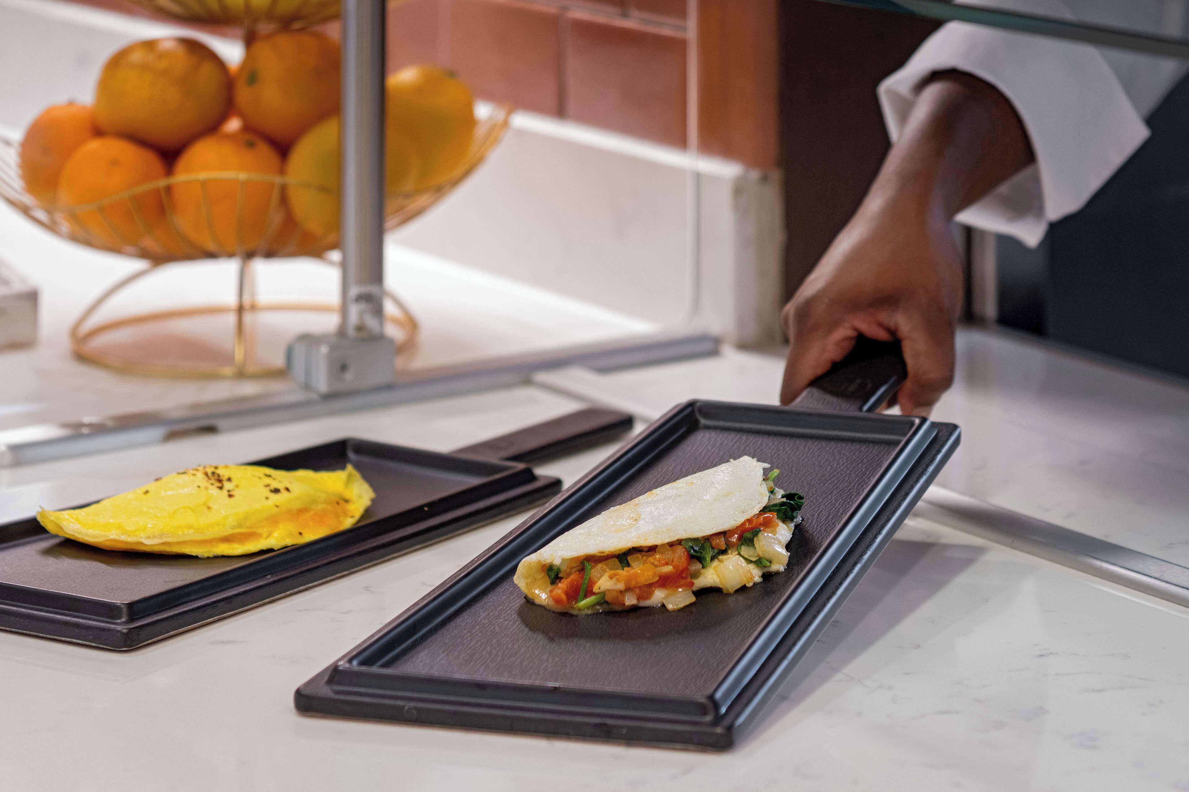 A buffet setup with a variety of food items, including a dish with a rolled omelette and another with a vegetable wrap.