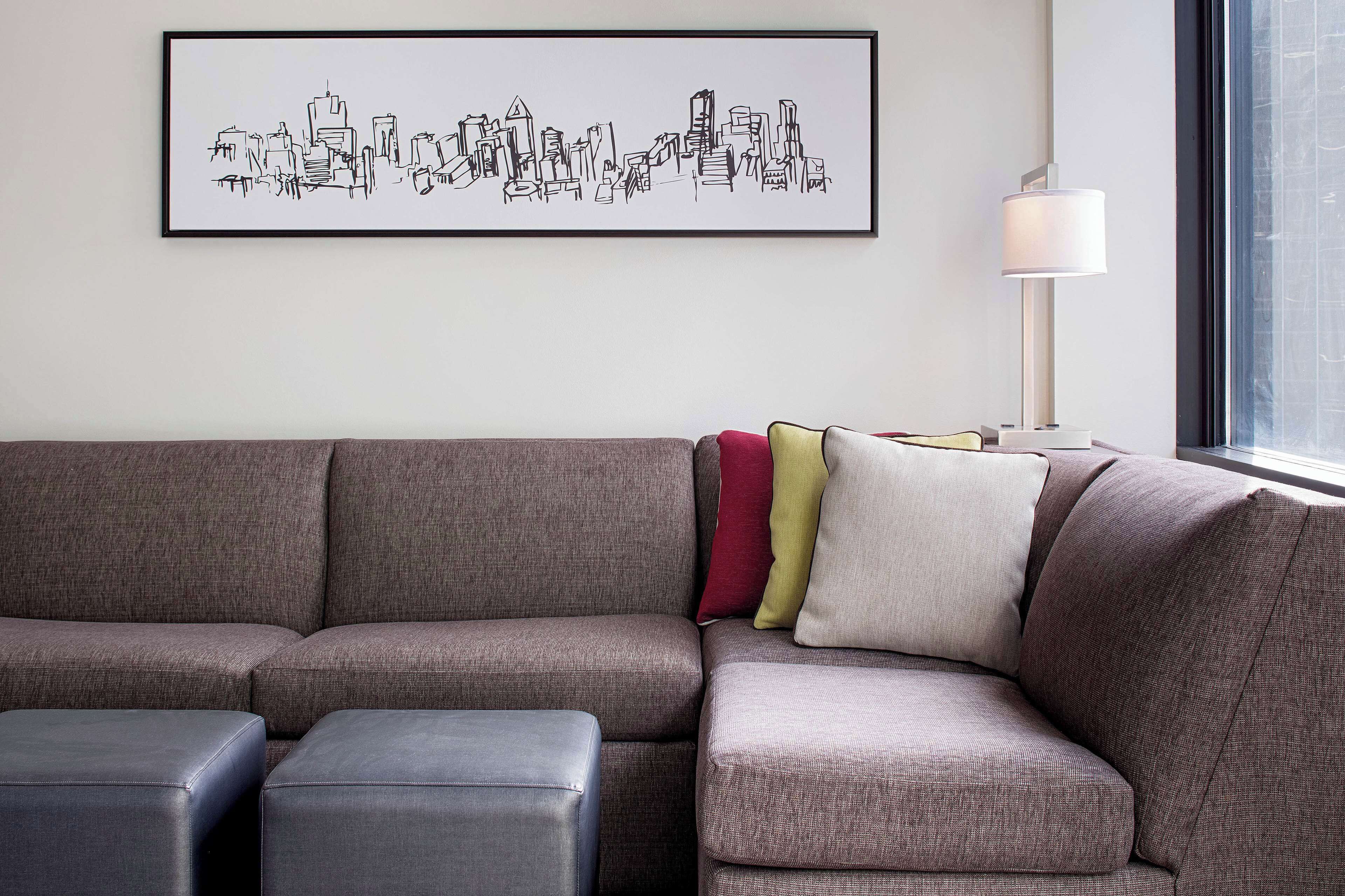 A sectional sofa with multiple cushions, a framed cityscape artwork, and a floor lamp.