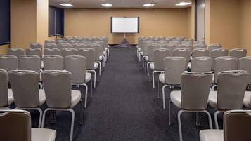 Uma sala de conferência com fileiras de cadeiras voltadas para uma tela de projeção vazia.