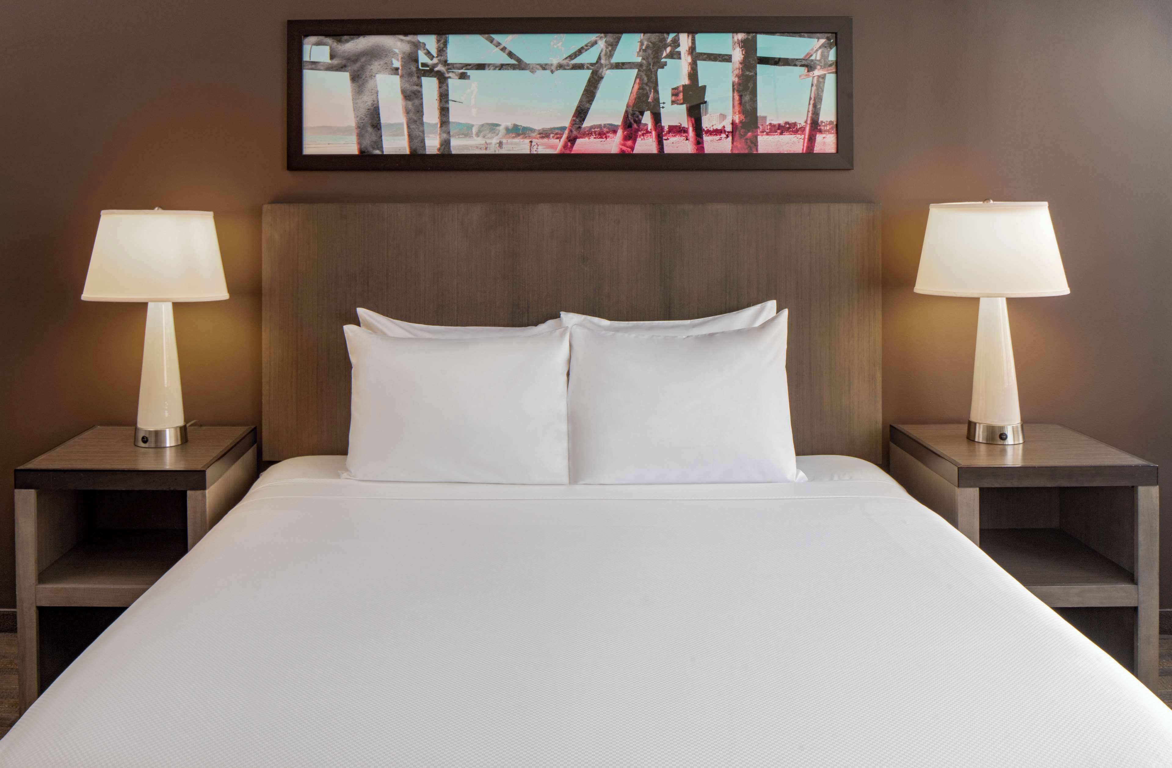 A hotel room with a large bed, two bedside tables with lamps, and a framed picture on the wall.