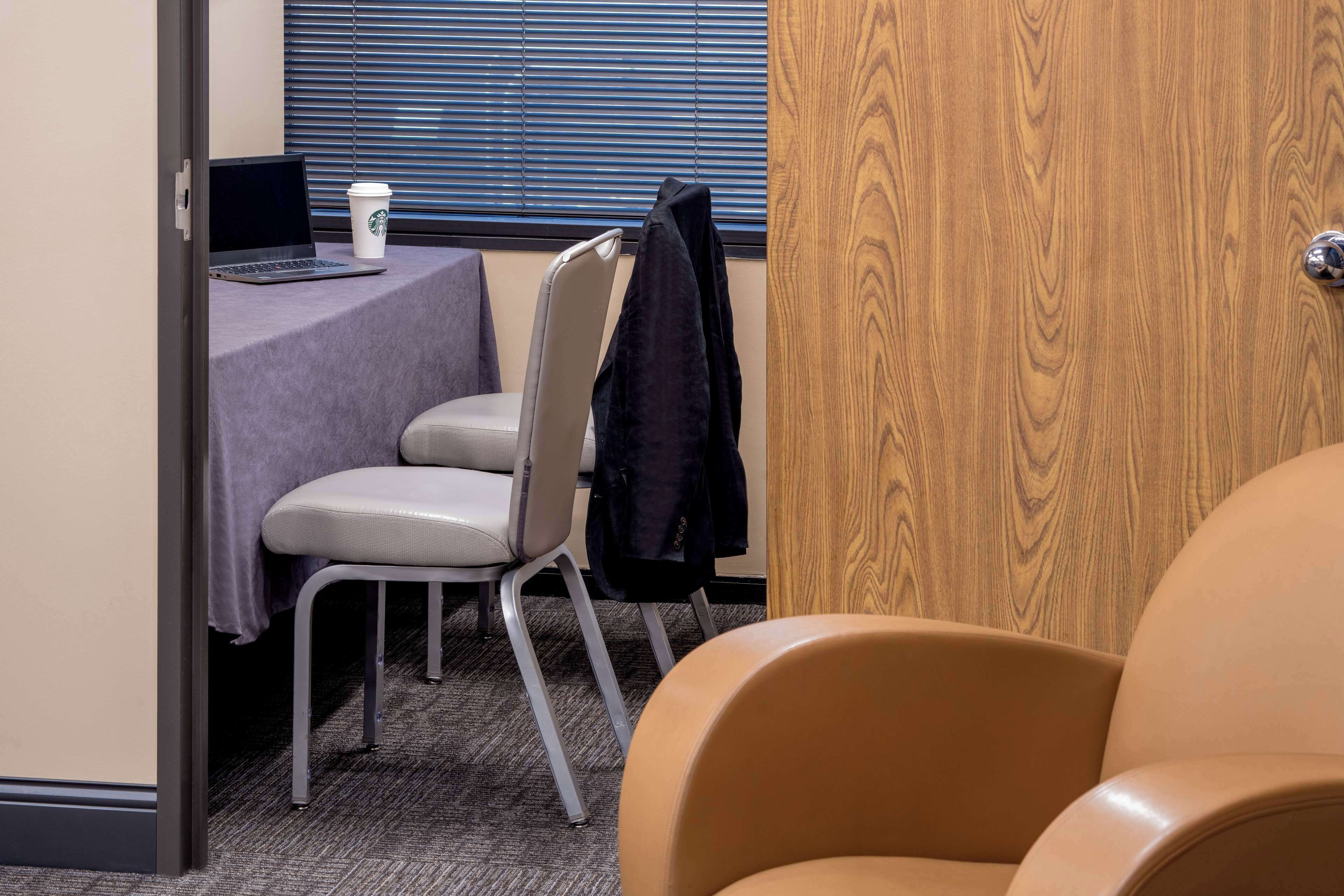 A hotel room with a desk, a laptop, a coffee cup, and a chair.