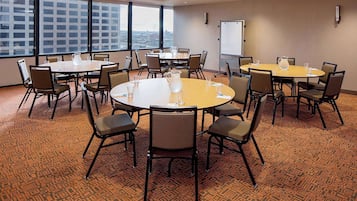 A conference room with multiple tables and chairs, large windows with a city view, and a whiteboard on the wall.