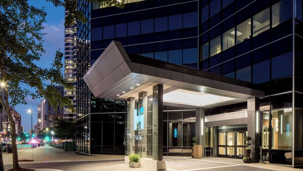Une entrée d’hôtel moderne avec une façade en verre, un espace d’entrée abrité et un hall d’accueil bien éclairé.