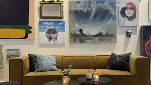 A living room with a mustard-colored sofa, two round coffee tables with candles, and various framed artworks on the walls.