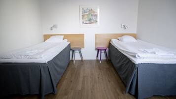 Een kamer met twee bedden, een houten hoofdbord, een klein krukje en een wandlamp.