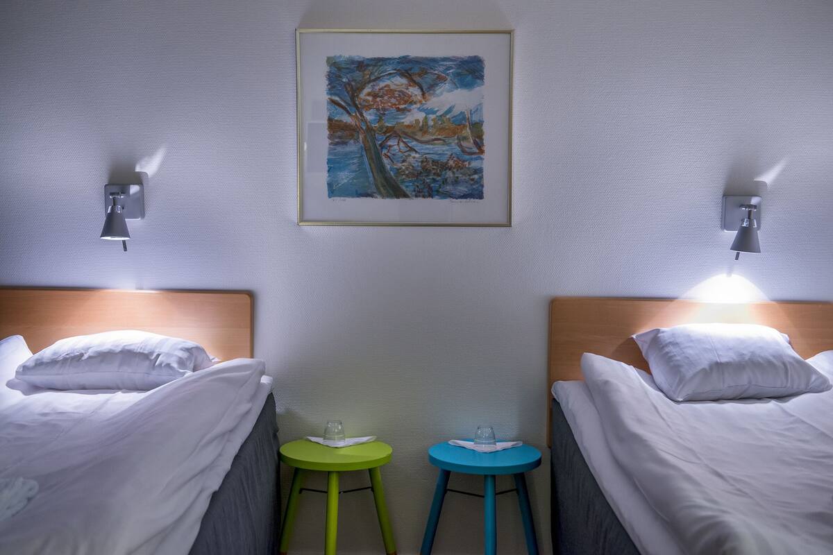 Ein Hotelzimmer mit zwei Betten, einem Bild an der Wand und zwei kleinen Hocker.