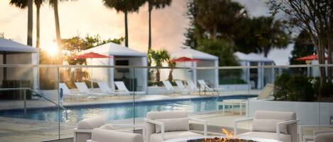 A poolside area with lounge chairs, a fire pit, and a glass railing overlooking a pool.