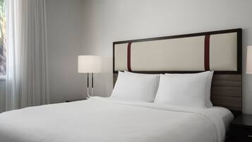 A neatly made bed with white linens, a wooden headboard, and two bedside lamps.