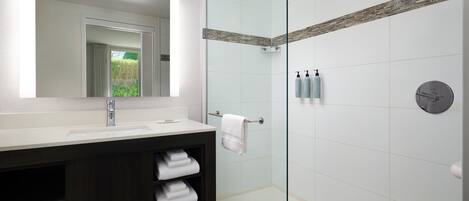 A modern bathroom with a glass-enclosed shower, a large mirror, and a dark wooden vanity.