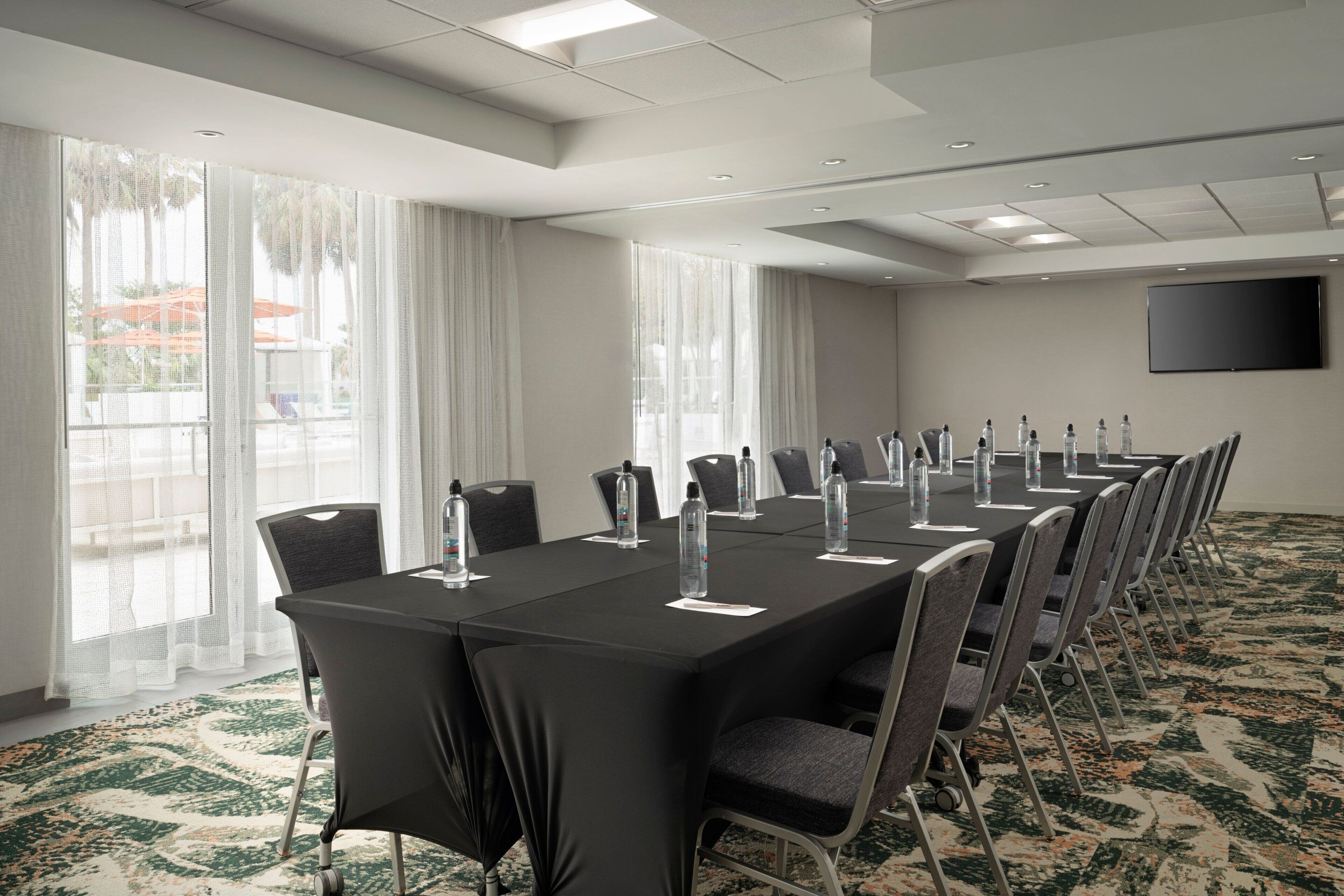 A conference room with a long table, chairs, water bottles, and a TV on the wall.