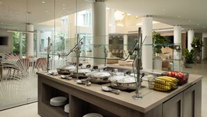 Un buffet moderne, aménagé avec des cloisons en verre, des plats et ustensiles de service en acier inoxydable, et une grande variété de fruits et de légumes.