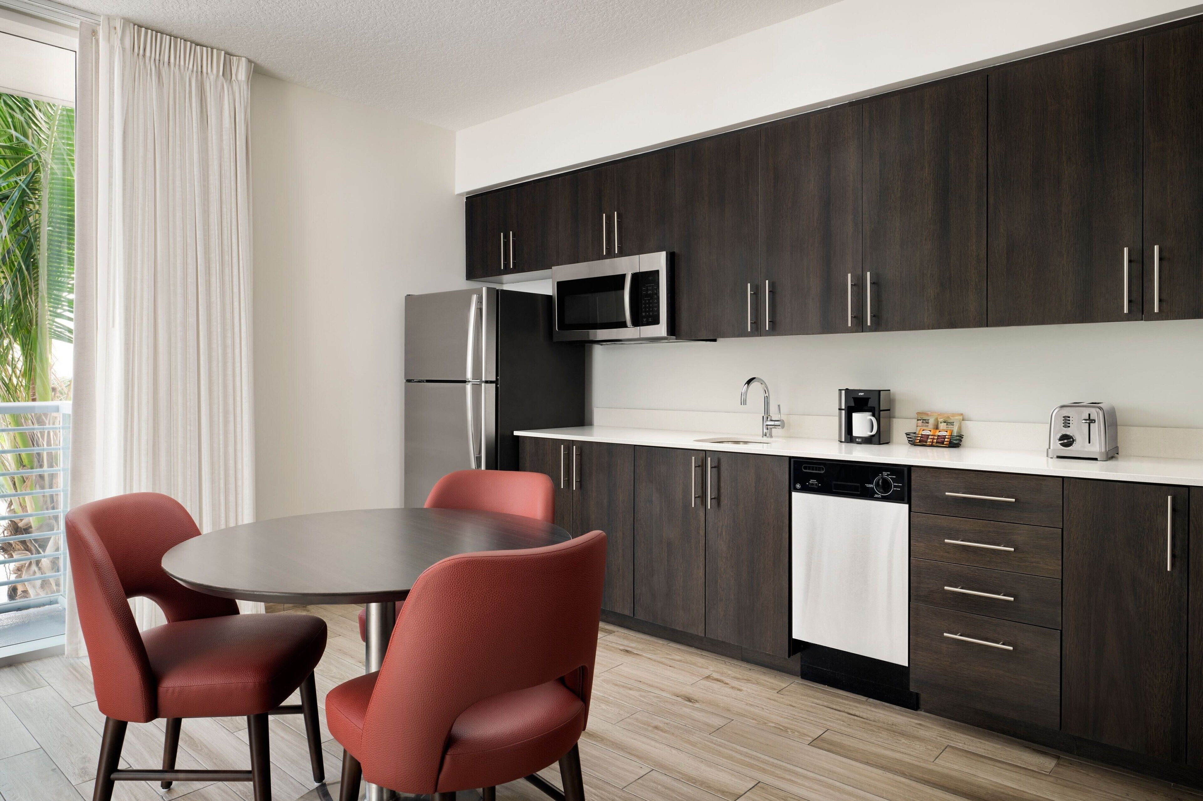 Une cuisine moderne avec des meubles de couleur bois foncé, des appareils en acier inoxydable et une table de salle à manger ronde entourée de chaises rouges.