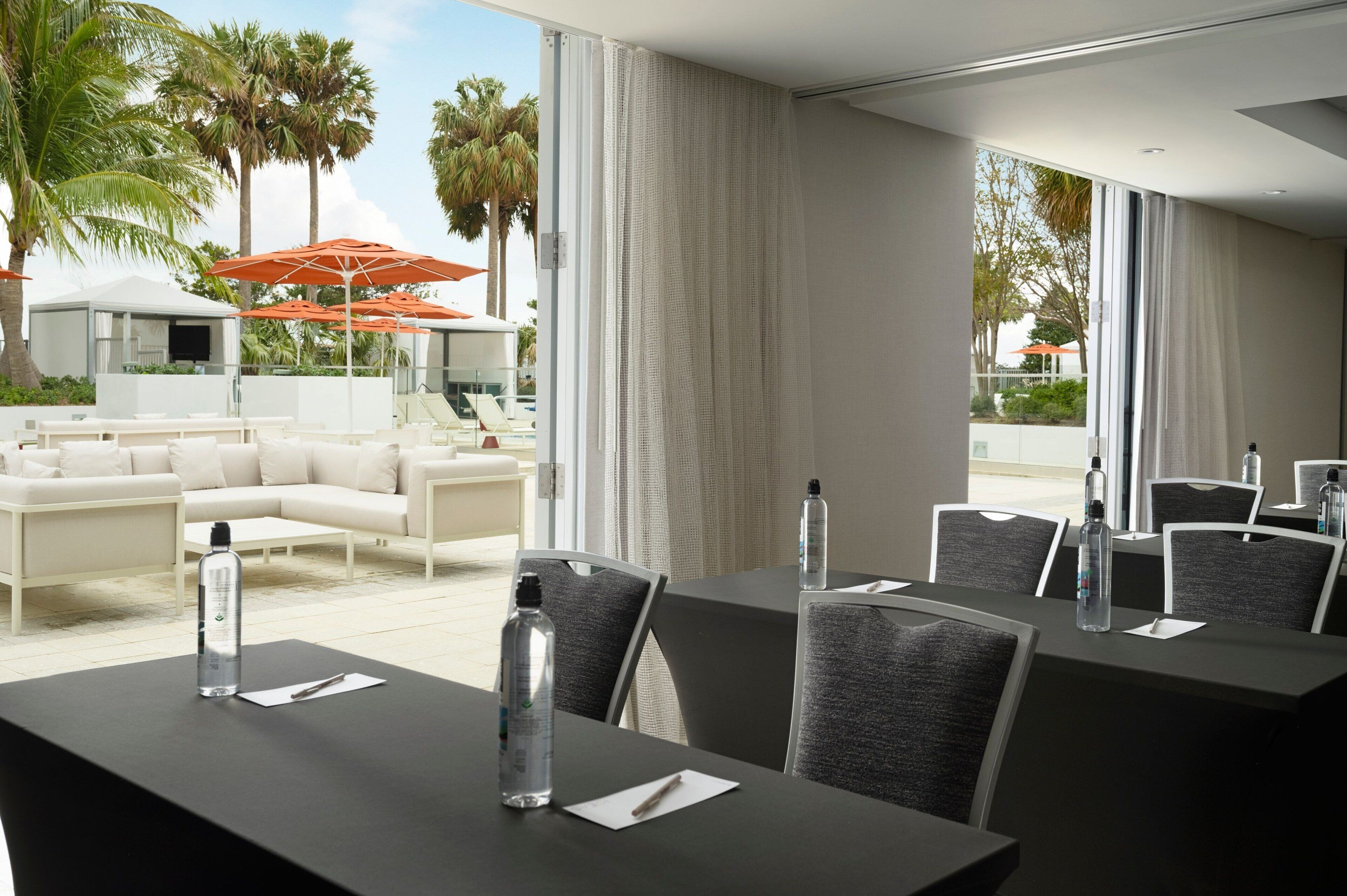 A hotel room with a balcony, a seating area with white sofas, and a dining area with tables and chairs.