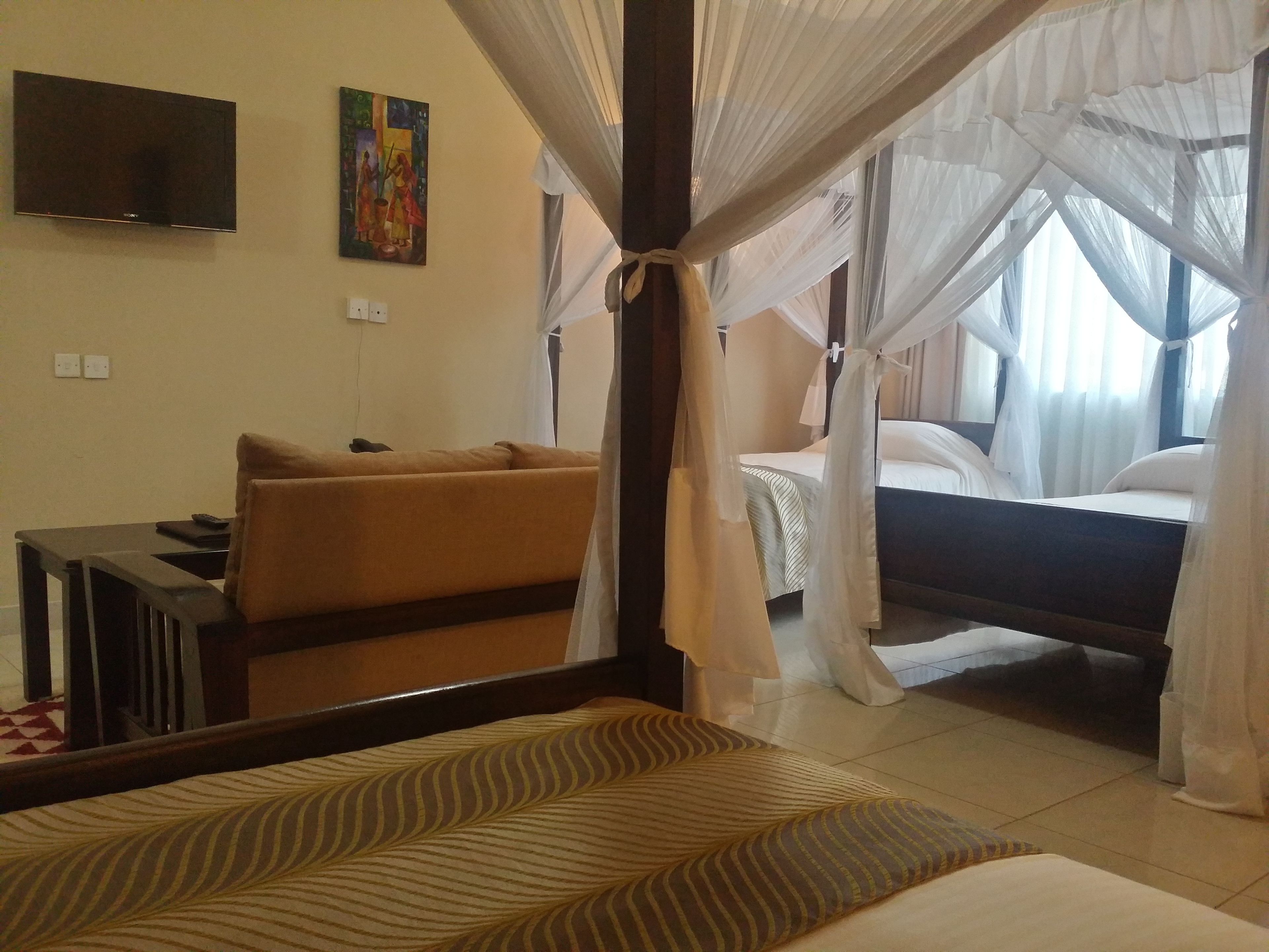 Una habitación de hotel con cama, sofá, televisor y un cuadro en la pared.