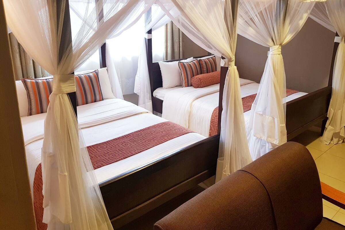 A hotel room with four beds, each with white bedding and red accents. The beds are arranged in a row with a canopy over each.