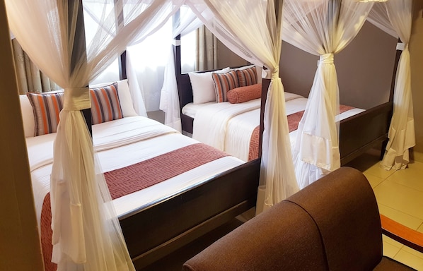 Een hotelkamer met vier bedden, elk voorzien van witte lakens en rode accenten. De bedden staan in een rij, elk met een hemelbed erover.