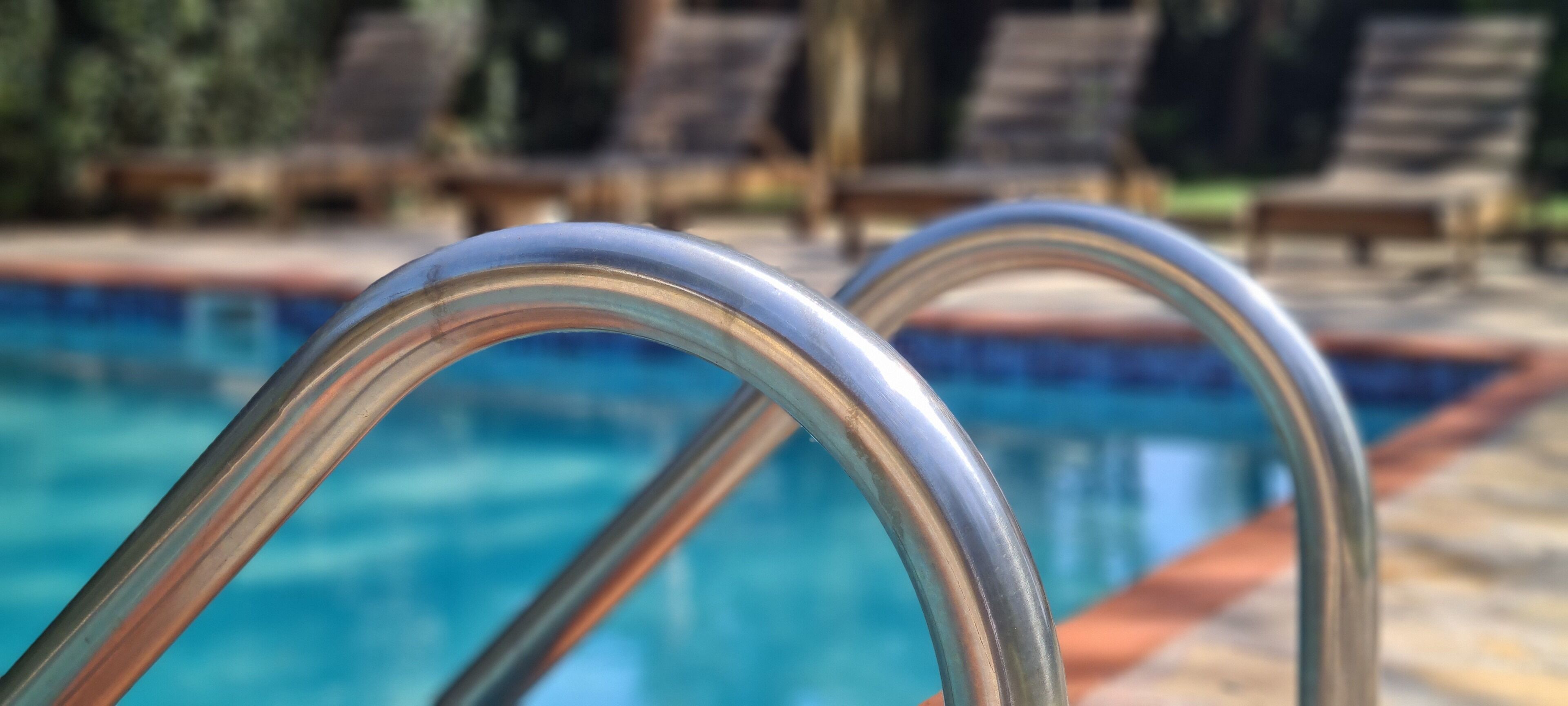 Una piscina con barandillas de metal y sillones de descanso al fondo.